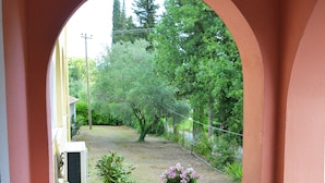 Un portico coperto con tavolo e sedie, una pianta in vaso e vista su un giardino attraverso un arco.