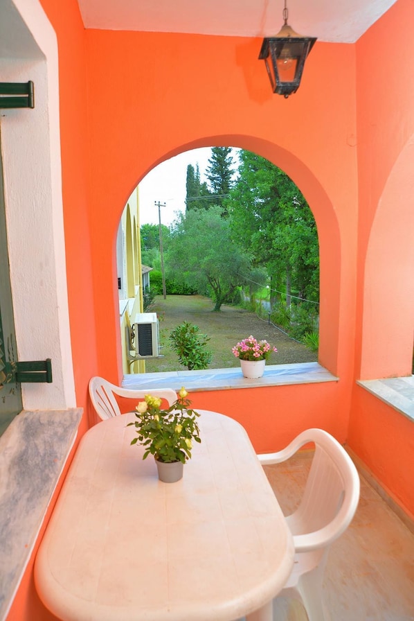 A room with a white table and chairs, a window with an arch, and a view of greenery outside.