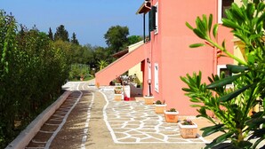 Un sentiero conduce a un edificio con facciata rossa, piante in vaso e cielo sereno.