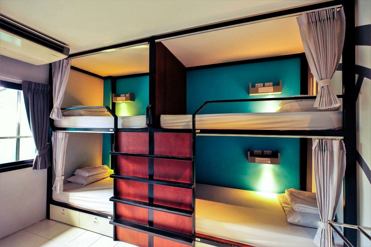 A bunk bed room with a window, curtains, and a wall-mounted shelf.