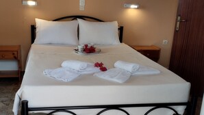 Un letto rifatto con lenzuola bianche, un vassoio con due tazze e fiori rossi, e un comodino in legno con un cassetto.