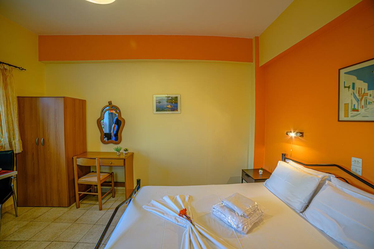A hotel room with a bed, a desk, a chair, a wardrobe, and a painting on the wall.