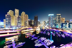 Un puerto deportivo con barcos amarrados, un horizonte urbano con edificios iluminados y un puente que conecta dos zonas.