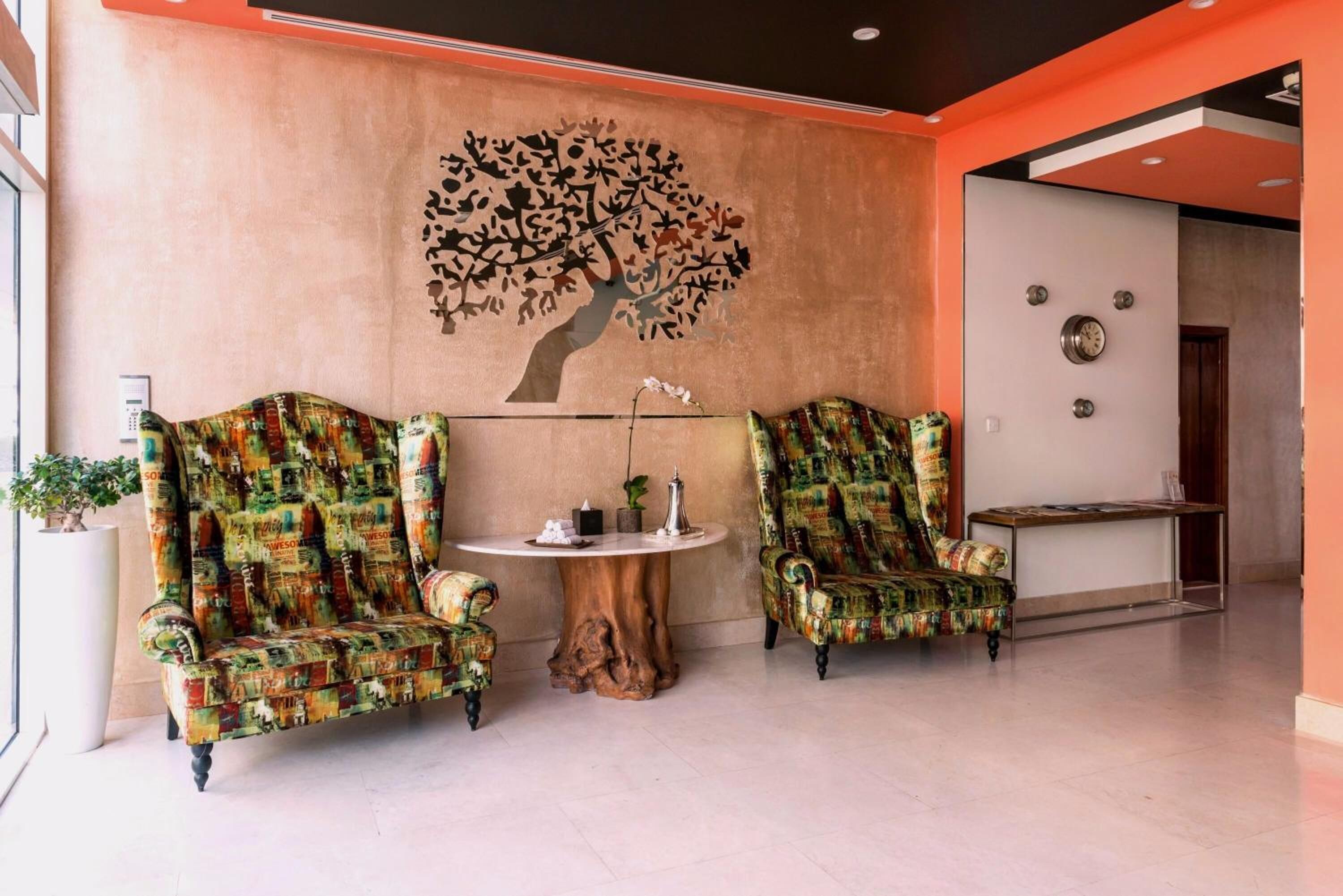 A lobby with two patterned armchairs, a round wooden table, and a wall-mounted clock.