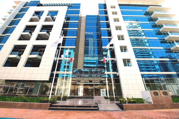 Un edificio moderno con fachada de vidrio, varios pisos y una entrada central con escalones.
