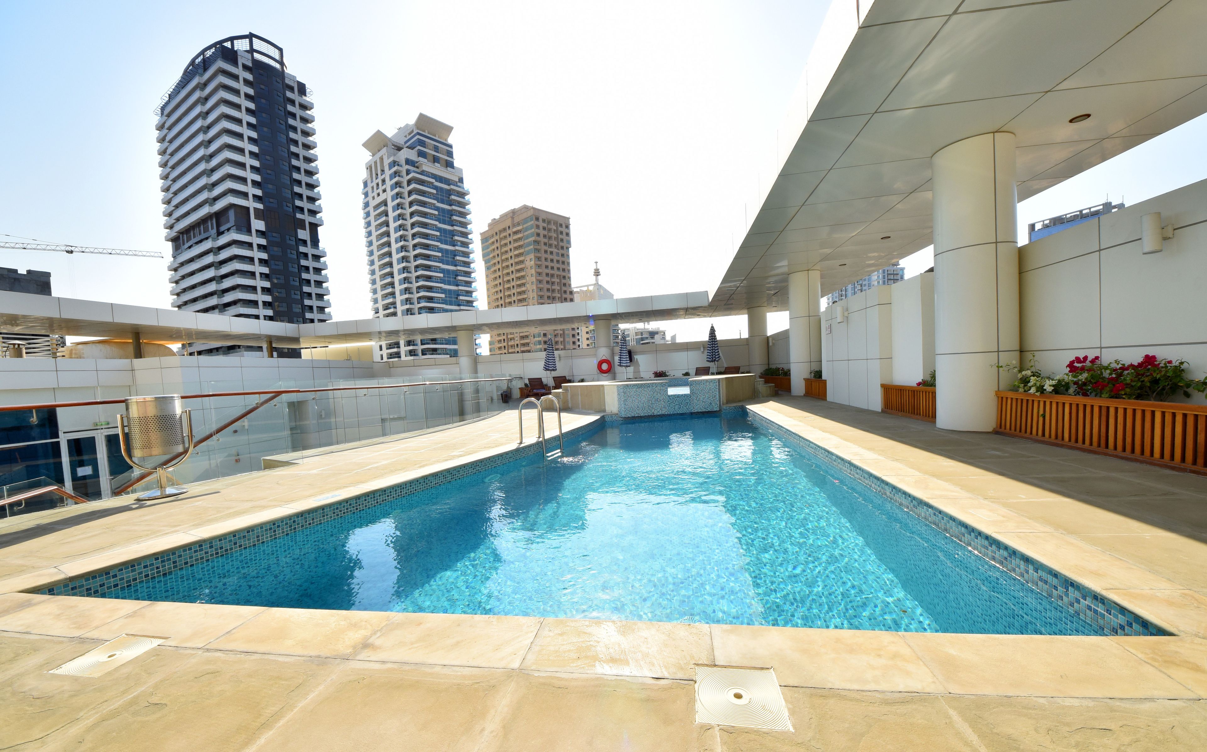 A rooftop pool with clear blue water, surrounded by a tiled deck and a glass railing.