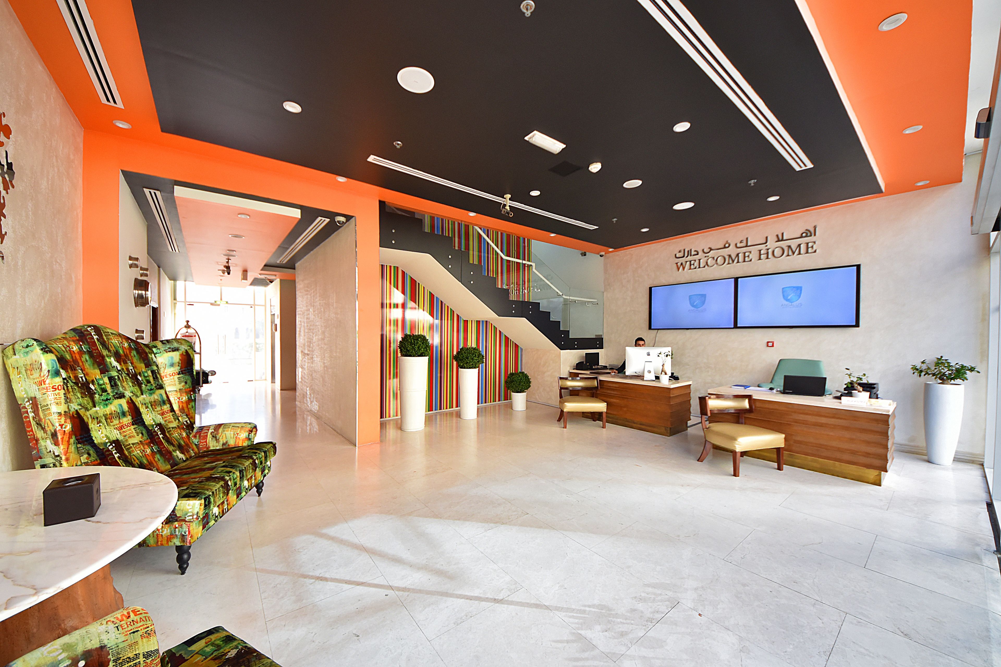 A modern reception area with a reception desk, seating, a staircase, and a large sign that reads "WELCOME HOME".