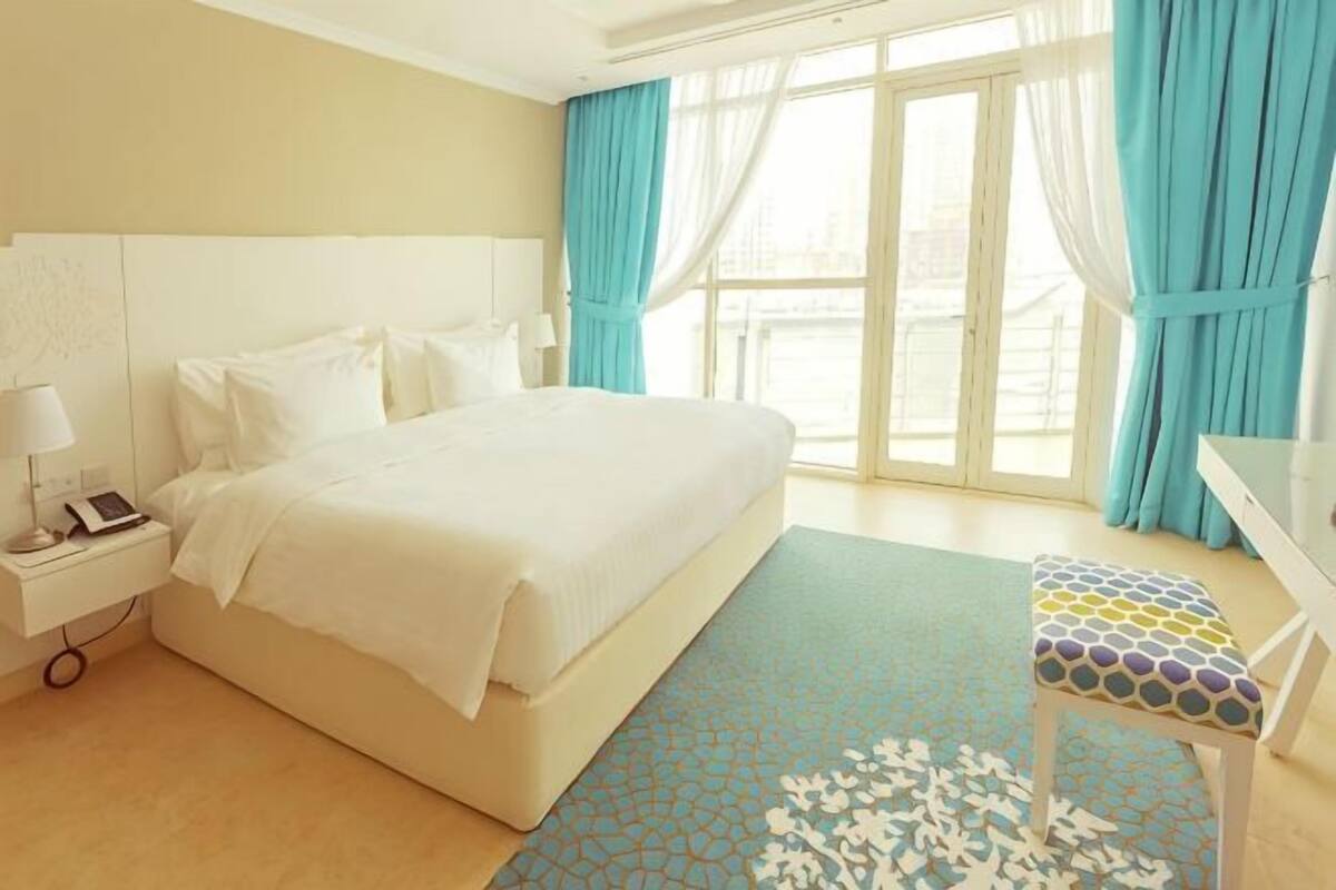 Een hotelkamer met een groot bed, een nachtkastje met lamp, een bureau met stoel en uitzicht door de glazen deuren.