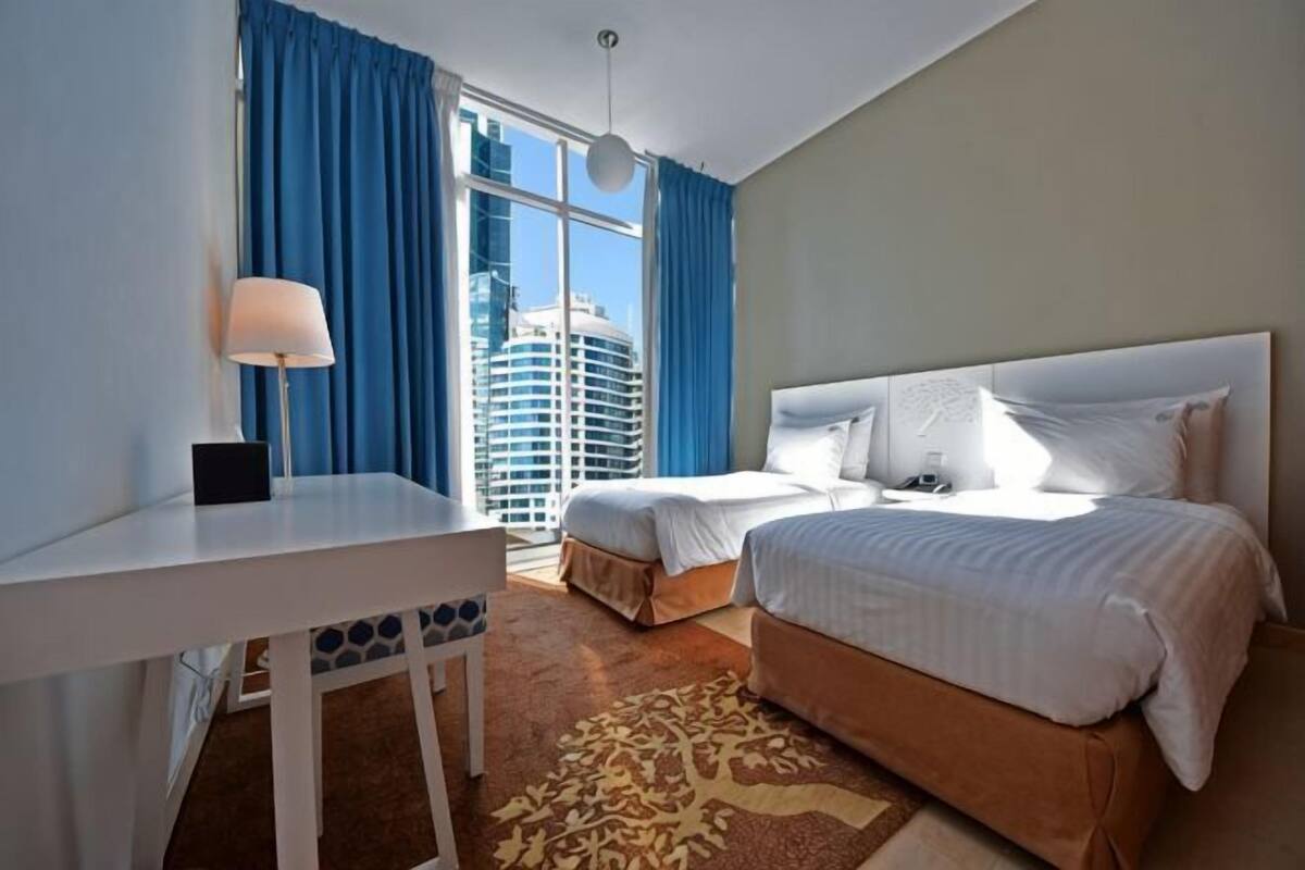Hotelkamer met een bed, een bureau, een stoel, een raam met gordijnen en uitzicht op een gebouw.