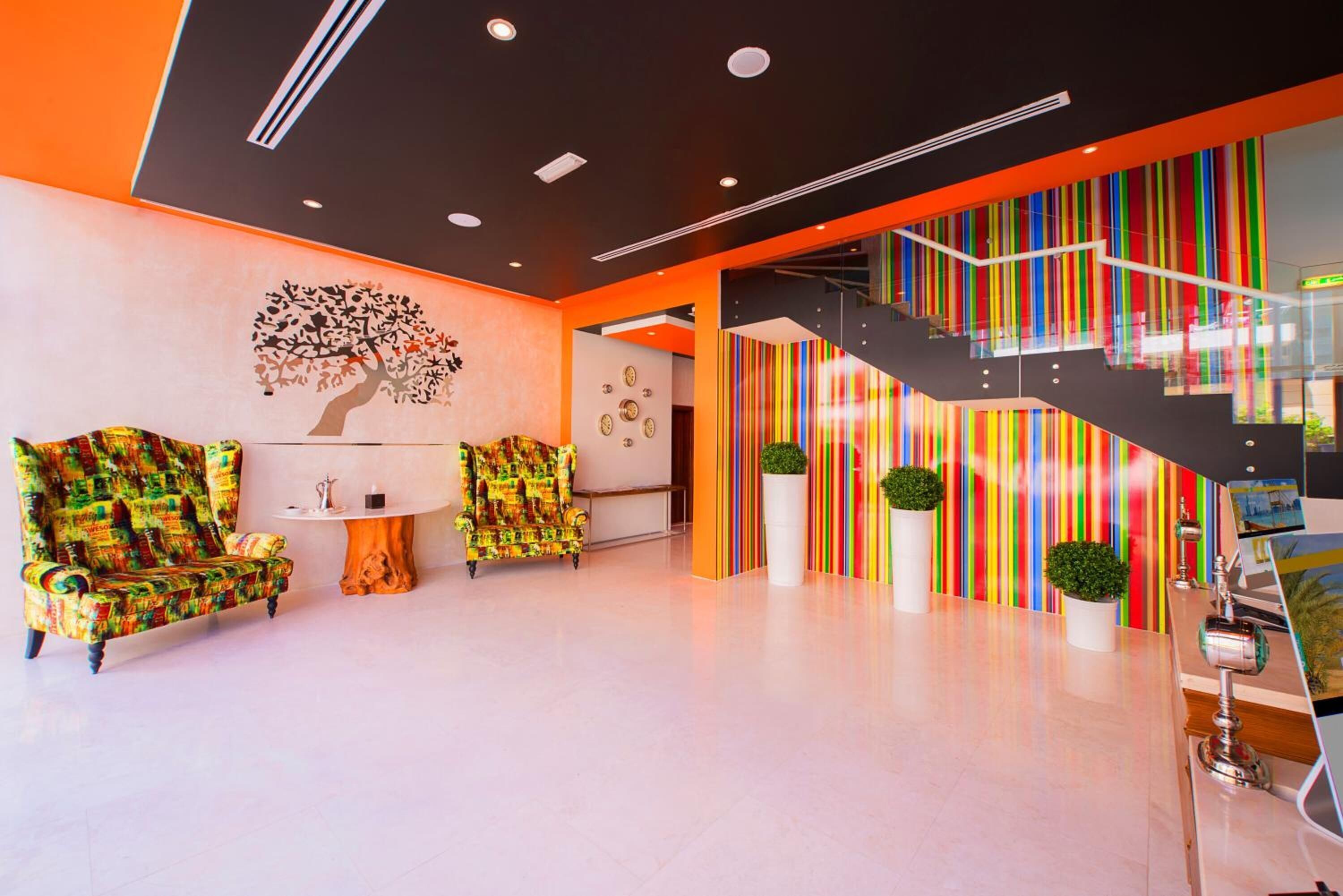 Un vestíbulo moderno con una escalera, pared con rayas de colores y dos sillas estampadas.