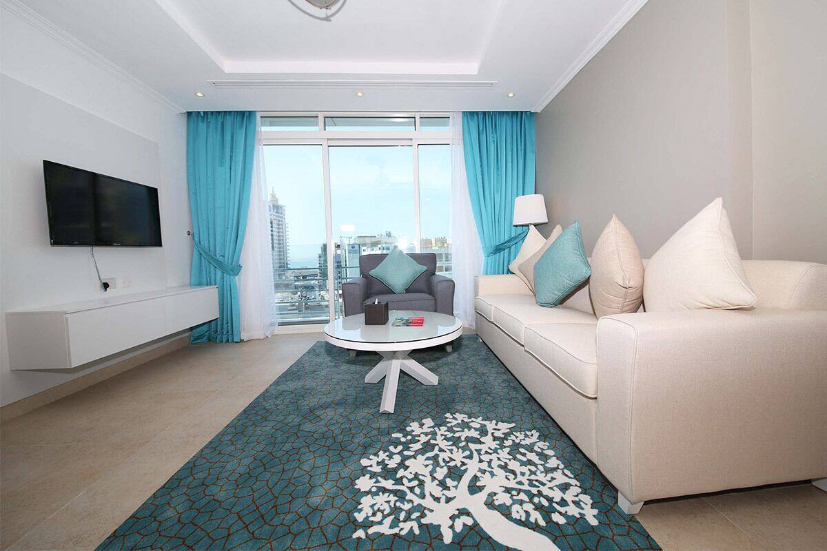 Una habitación de hotel moderna con un ventanal grande, un televisor de pantalla plana, una mesa de centro redonda, un sofá y una alfombra estampada.