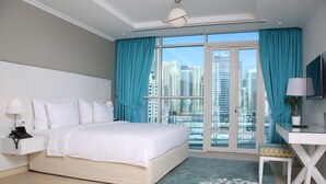 A modern hotel room with a large bed, a desk, a chair, and a view of tall buildings.