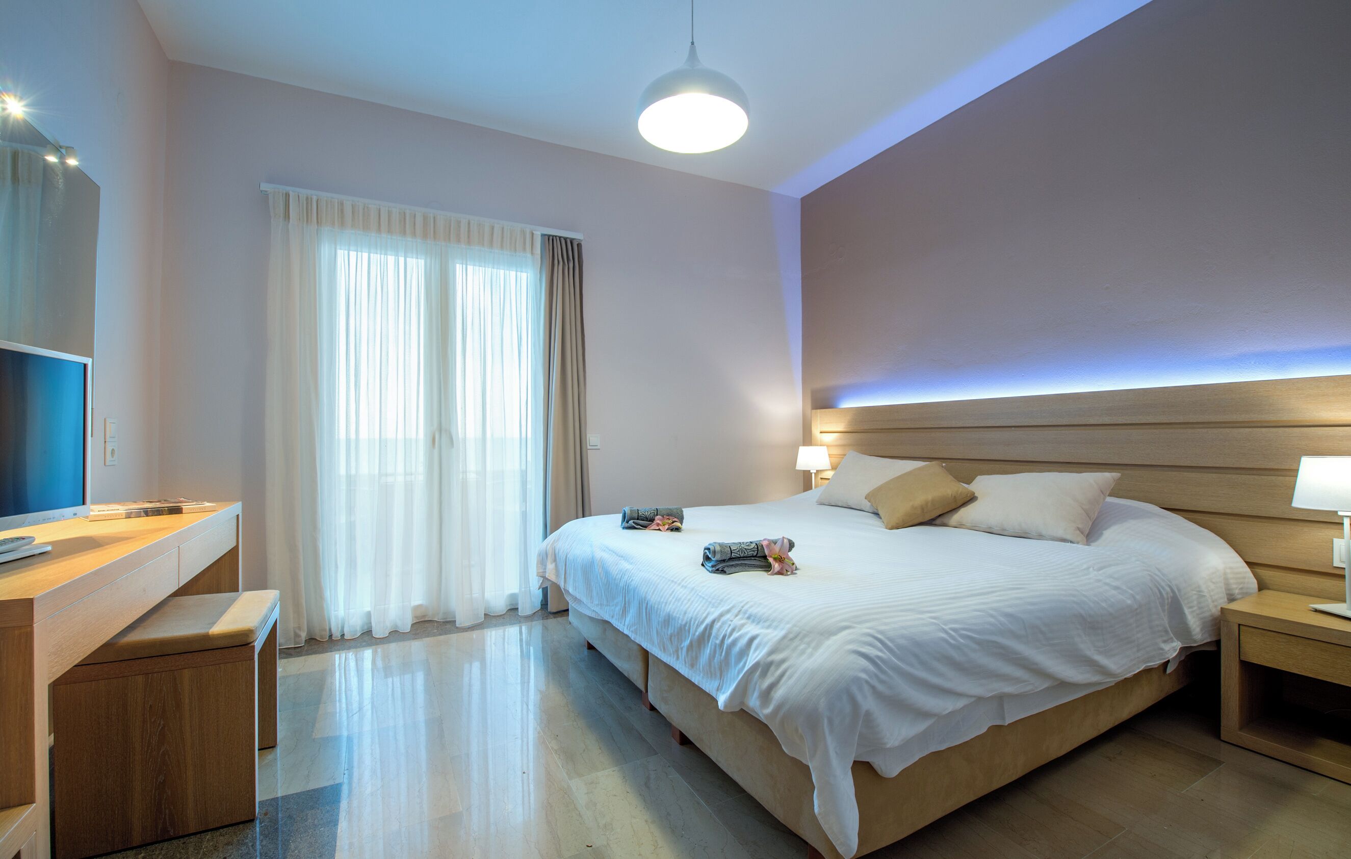 A modern hotel room with a large bed, bedside tables, a desk with a chair, and a television.