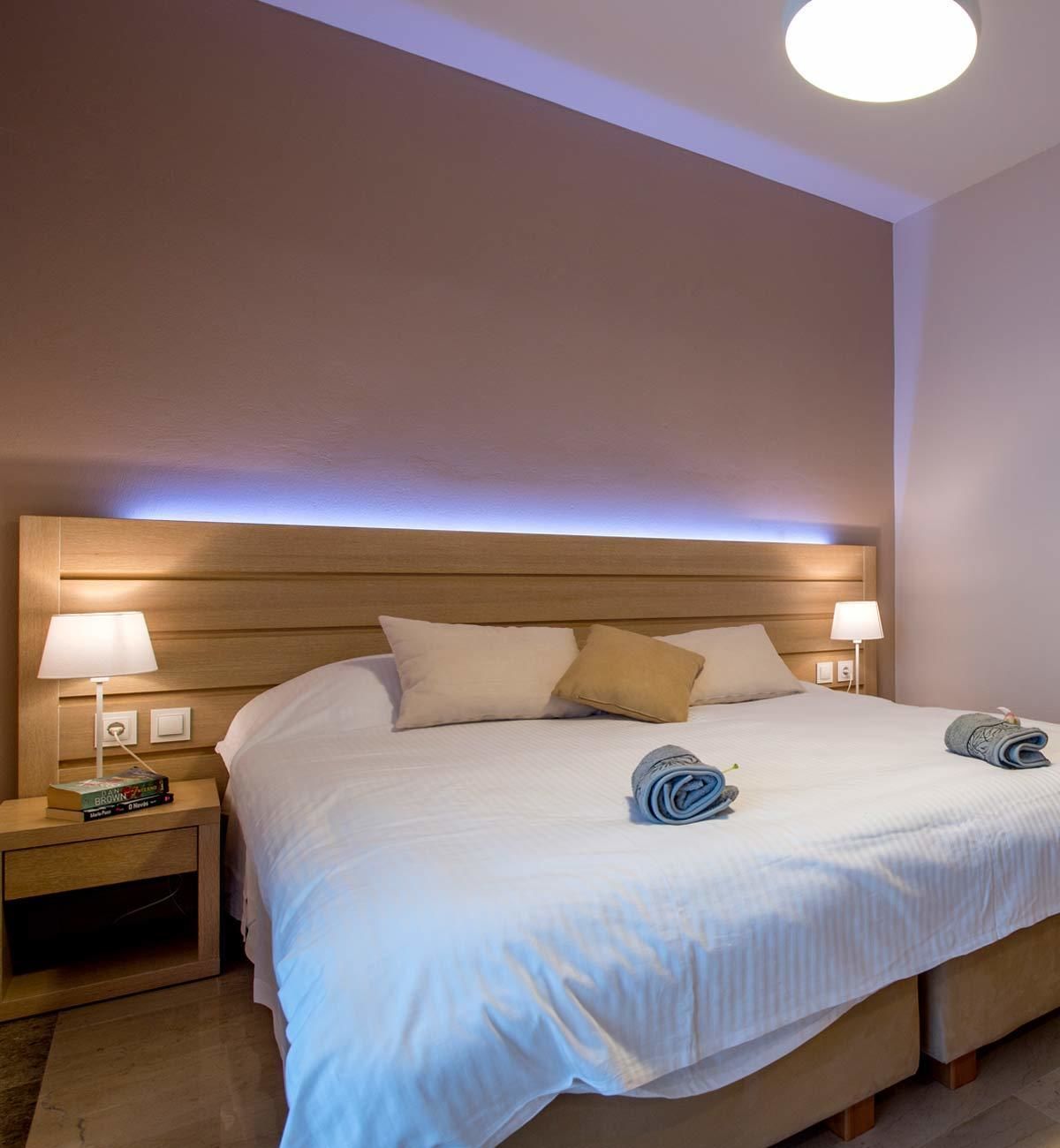 A neatly made bed with white linens, two bedside lamps, and a wooden headboard.