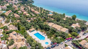 An aerial view of a coastal residential area with a swimming pool, houses, and a beach. - Barbati Beach Apartments (Corfu)