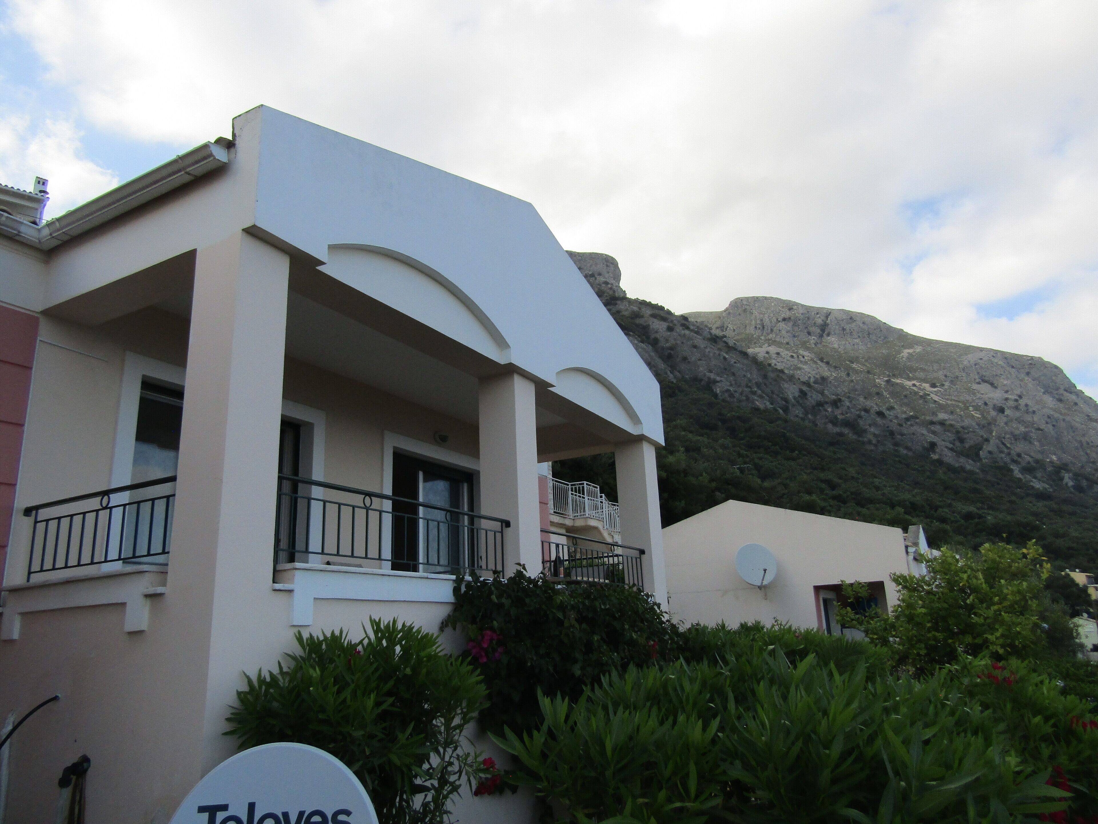 A modern building with a balcony, a satellite dish, and a mountainous backdrop.