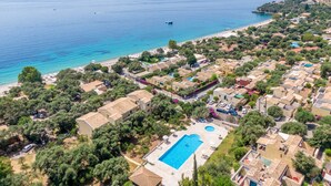 An aerial view of a coastal residential area with a swimming pool, beach, and clear blue sea. - Barbati Beach Apartments (Corfu)