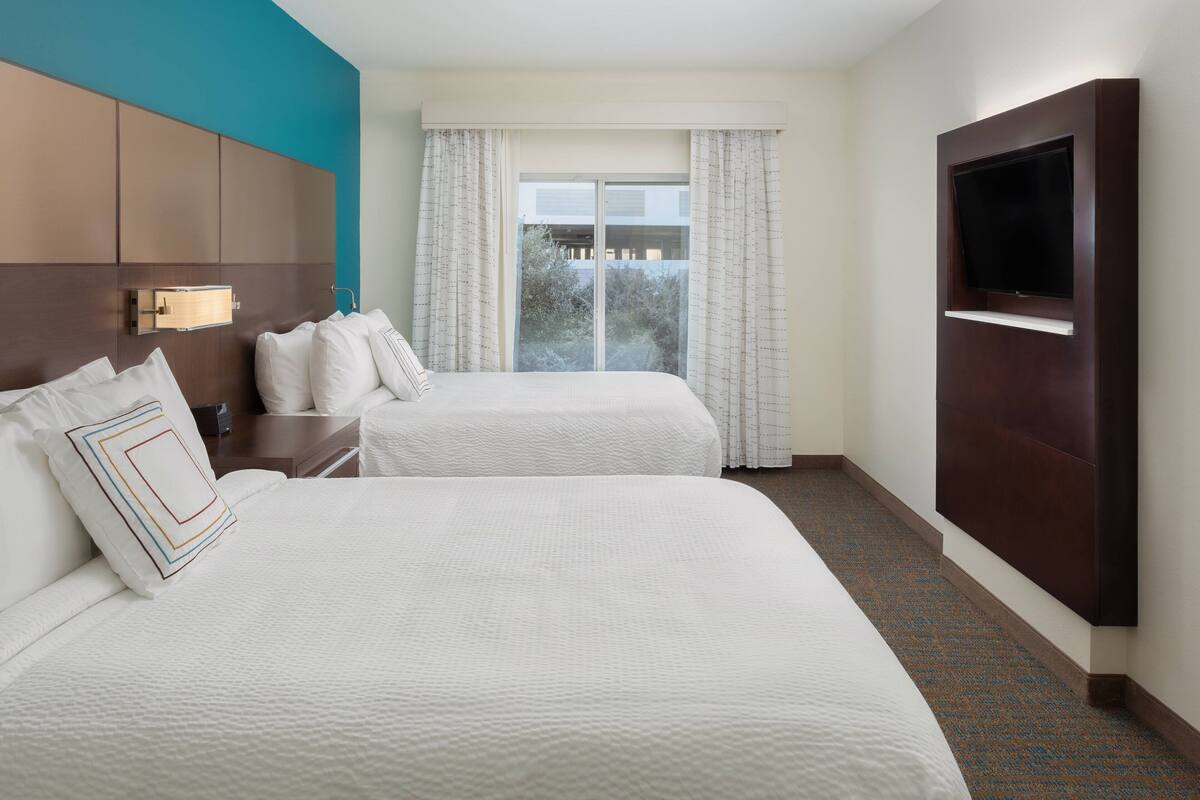 A hotel room with two beds, a TV mounted on the wall, and a window with curtains.