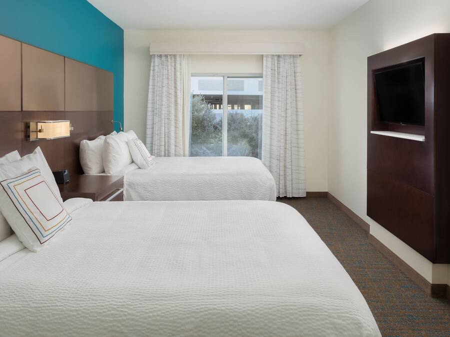 A hotel room with two beds, a TV mounted on the wall, and a window with curtains.