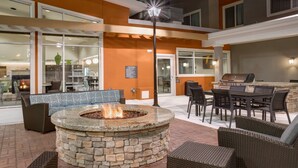 A stone fire pit surrounded by wicker furniture, a grill, and a dining area with chairs and tables.