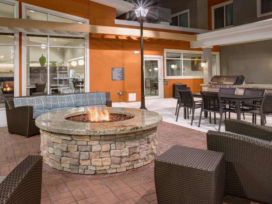 Un foyer en pierre entouré de meubles en osier, un barbecue et un espace repas avec des chaises et des tables.