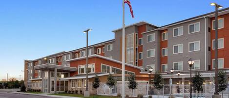 A multi-story hotel with a flagpole, outdoor lighting, and a fenced pool area.