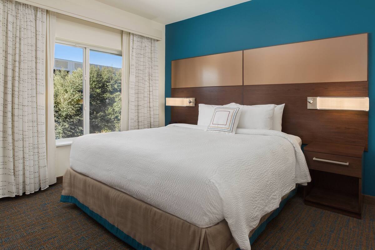 A hotel room with a large bed, a nightstand, and a window with curtains.