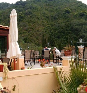 An outdoor seating area with tables and chairs, overlooking a lush green hillside. - Alonakia Hotel (Corfu)