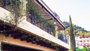 Un edificio de dos pisos con un balcón, rodeado de follaje y un jardín.