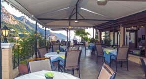 An outdoor patio with tables and chairs, surrounded by potted plants and a mountain view. - Alonakia Hotel (Corfu)