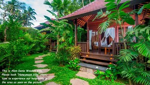 A wooden villa with a covered porch, surrounded by lush greenery and palm trees. - Alam Dania Cottage (Ubud)