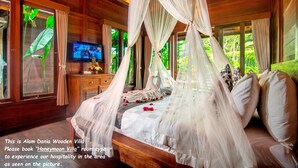 A wooden villa bedroom with a canopy bed, a television, and a view of lush greenery. - Alam Dania Cottage (Ubud)