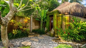 A tropical garden with a thatched-roof structure, a stone pathway, and lush greenery. - Alam Dania Cottage (Ubud)