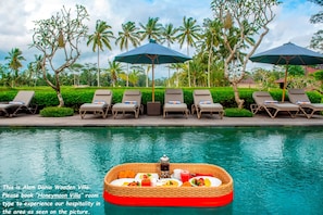 A poolside view with lounge chairs and umbrellas, a floating breakfast tray, and a tropical setting with palm trees. - Alam Dania Cottage (Ubud)