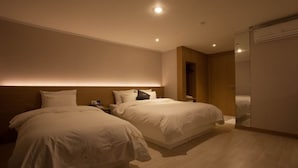 A hotel room with two beds, a wooden headboard, a wardrobe, and a bedside table with a lamp. - Vatica Hotel Dongdaemun (Seoul)
