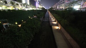 A nighttime view of a city street with a water channel, illuminated pathway, and buildings in the background. - Vatica Hotel Dongdaemun (Seoul)