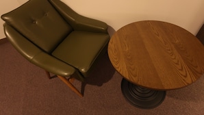 A green leather armchair and a round wooden table with a black base. - Vatica Hotel Dongdaemun (Seoul)