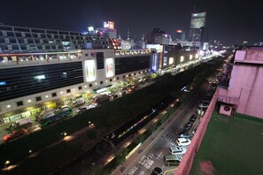 Un paisaje urbano nocturno con edificios iluminados, una calle concurrida y un espacio verde con un camino.