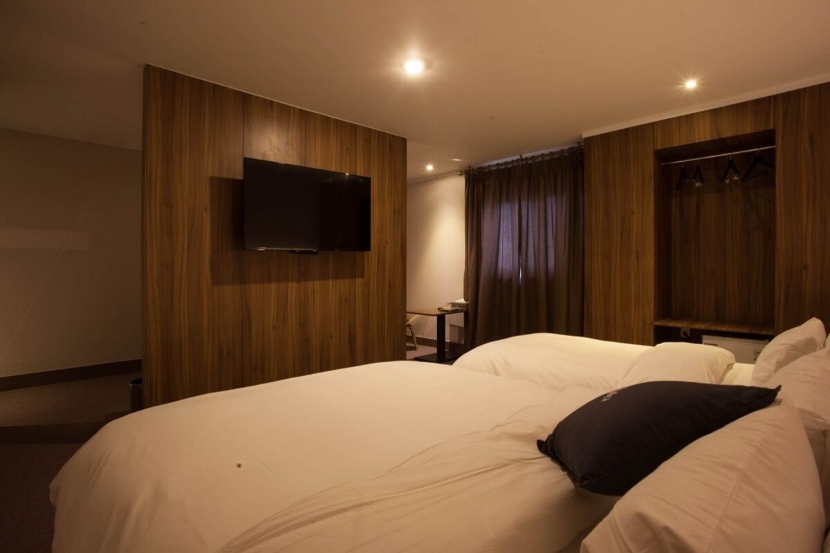 A hotel room with a large bed, a flat-screen TV mounted on the wall, and a wooden wardrobe.