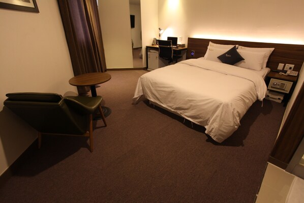 Habitación de hotel con cama, escritorio, silla, una mesita pequeña y mesita de noche con teléfono.