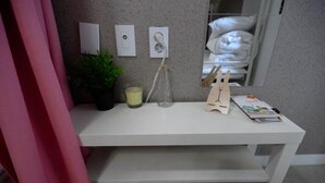 A white desk with a potted plant, a glass bottle, and a wooden toy. There are framed pictures on the wall and a white shelf below the desk. - Lombard House - Hostel (Seoul)