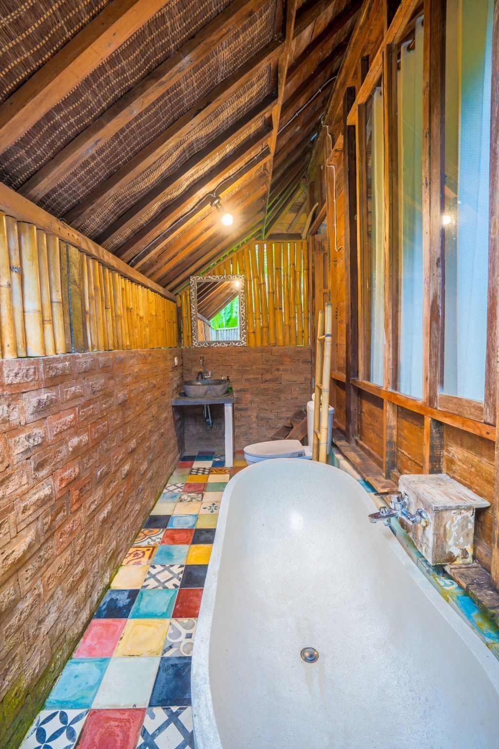 Ein schmales, rustikales Badezimmer mit einer großen Badewanne, Holzwänden und einem farbenfrohen Fliesenboden.