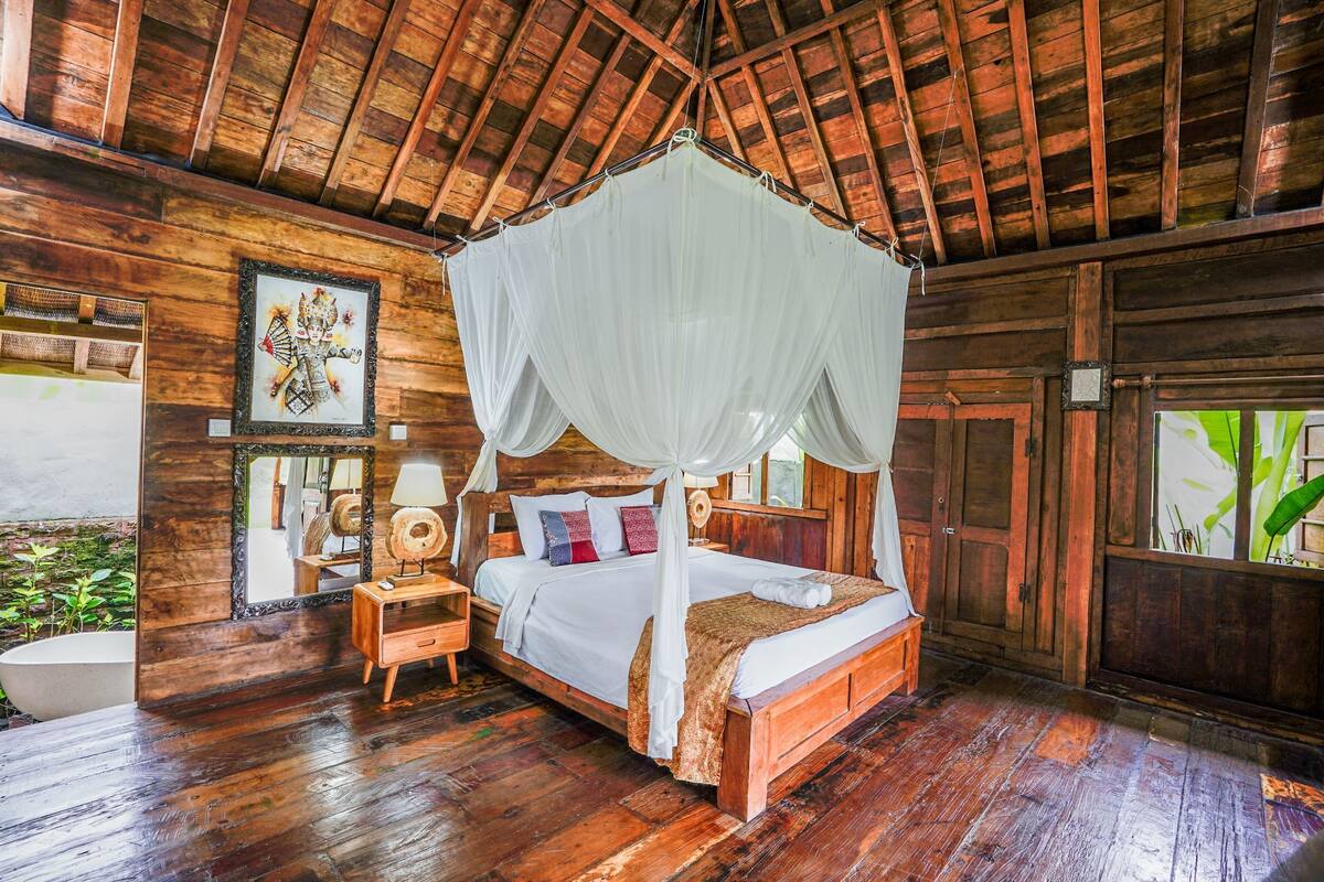 A wooden room with a four-poster bed, a nightstand, a mirror, and a wooden cabinet.
