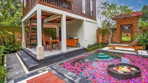 A two-story house with a balcony, a swimming pool surrounded by flower petals, and a dining area with a table and chairs.