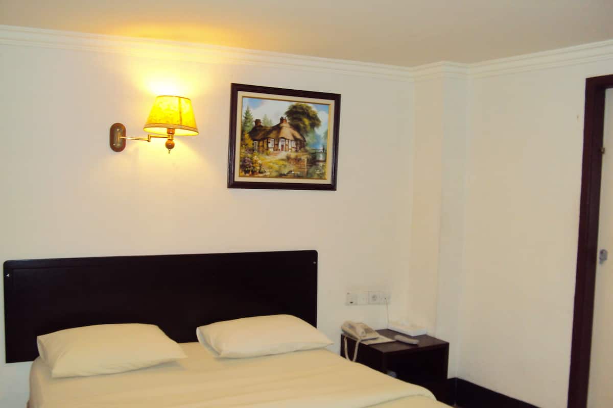 A hotel room with a bed, a bedside lamp, a painting on the wall, and a telephone on a nightstand.