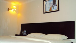 Una camera d'albergo con un letto, un comodino, un quadro appeso al muro e una lampada a parete.