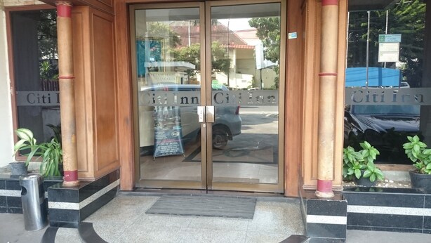 L'ingresso di un hotel con porte in vetro, una targa e piante in vaso.