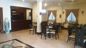 Un'area ristorazione con diversi tavoli e sedie, un angolo bar con televisore e un vaso decorativo.