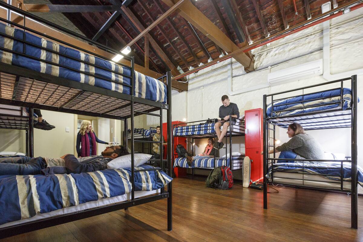Un dortoir avec des lits superposés, un plancher en bois et un plafond haut avec des poutres apparentes.