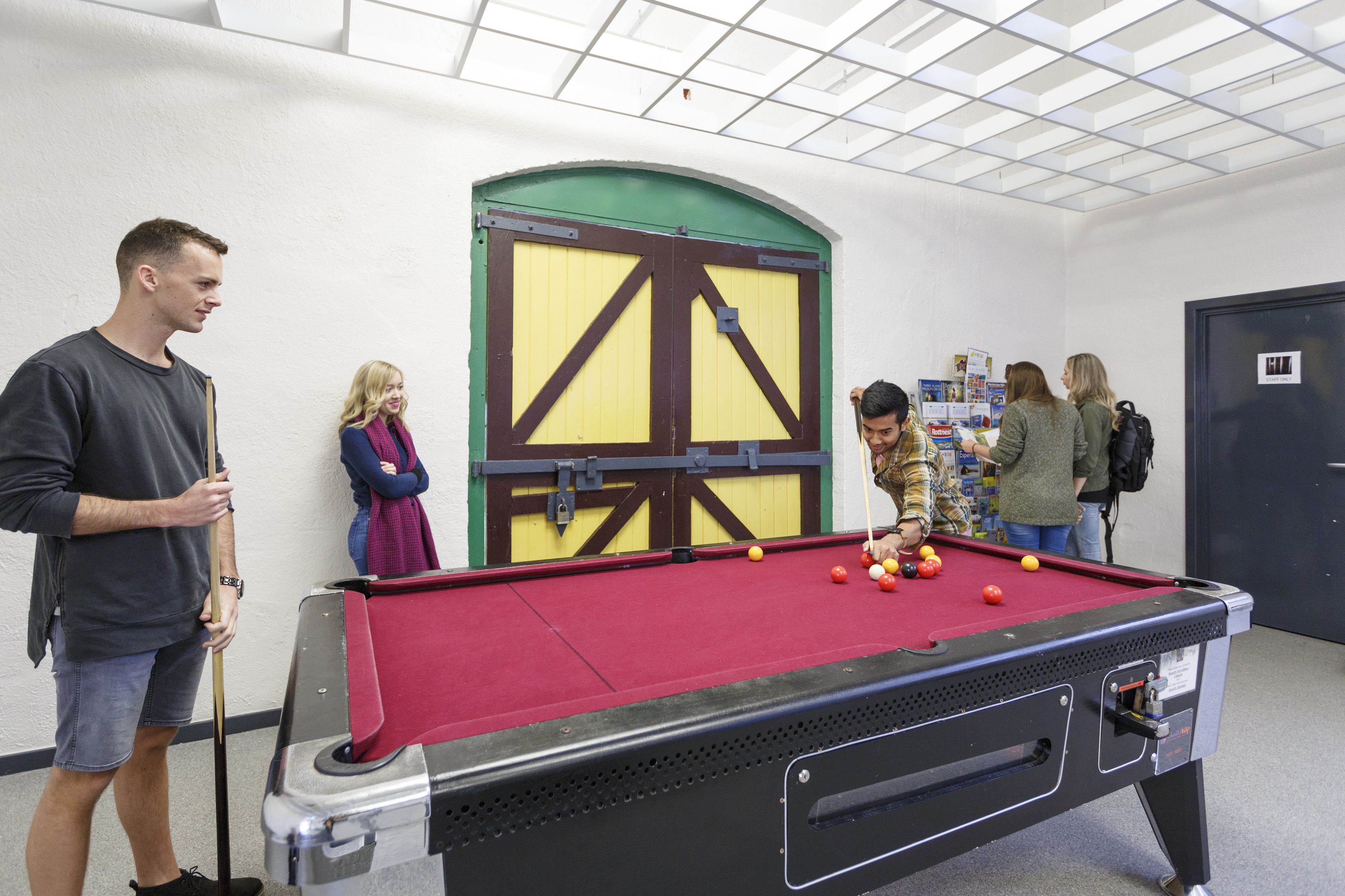 A pool table in a room with a white ceiling and walls, a green door, and a blue door.